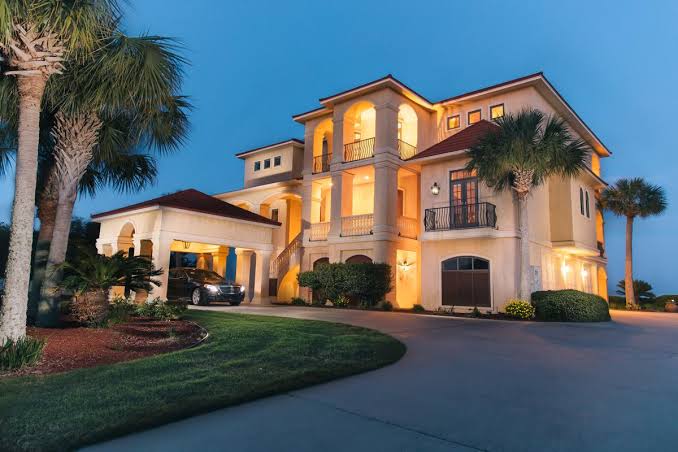 Three story estate home lit at dusk with a circular driveway
